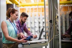 Two people looking at a laptop in an industrial setting.